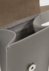 Interiér šedé kožené kabelky s hladkým povrchem, viditelným švem a patentním uzávěrem. Uvnitř je značka KIOMI.