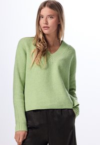 Ljusgrön ribbad tröja med V-ringning och långa ärmar, tillsammans med svarta byxor. Den strukturerade tyget ger visuell intresse.