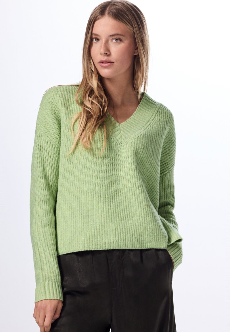 Ljusgrön ribbad tröja med V-ringning och långa ärmar, tillsammans med svarta byxor. Den strukturerade tyget ger visuell intresse.