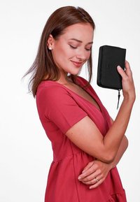 Black zippered wallet with textured surface held in a hand. Wallet features a subtle logo and a streamlined rectangular shape.