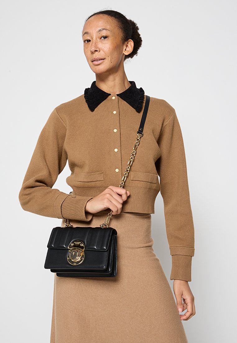 Braune, kurze Strickjacke mit schwarzem Kragen, cremefarbenen Knöpfen und geripptem Muster, kombiniert mit einer schwarzen Lederhandtasche mit goldenen Beschlägen.