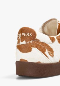 Zapatilla con estampado de vaca, texturizada en blanco y marrón, suela de goma marrón y logo "SCALPERS" en blanco en el talón.