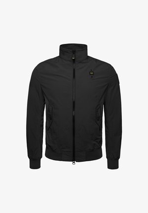 Schwarze Zip-Jacke mit hohem Kragen, Seitentaschen, elastischen Bündchen und einem strukturierten schwarzen Stoff. Mit einem kleinen gelben Logo auf der Brust.