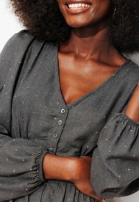 Robe grise avec un décolleté en V, de courtes manches bouffantes et un motif texturé. Comprend des boutons foncés et une taille froncée pour une coupe ajustée.