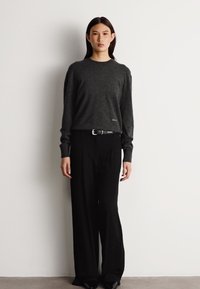 Grauer Pullover mit langen Ärmeln und Rundhalsausschnitt, kombiniert mit hoch sitzenden, schwarzen, weiten Hosen, die einen silbernen Schnallenakzent haben.