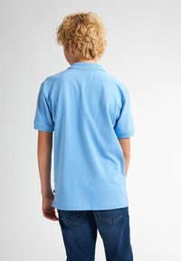 Světle modrá polo košile s krátkým rukávem, vybavená límcem a bočními rozparky, v kombinaci s tmavě modrými džíny. Měkký bavlněný materiál.