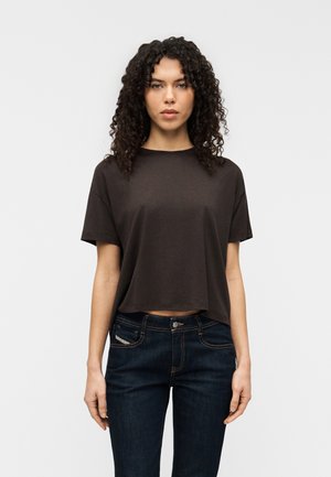 T-shirt marron raccourci à manches courtes, en tissu doux. Stylé avec un jean en denim foncé, coutures visibles et poches.