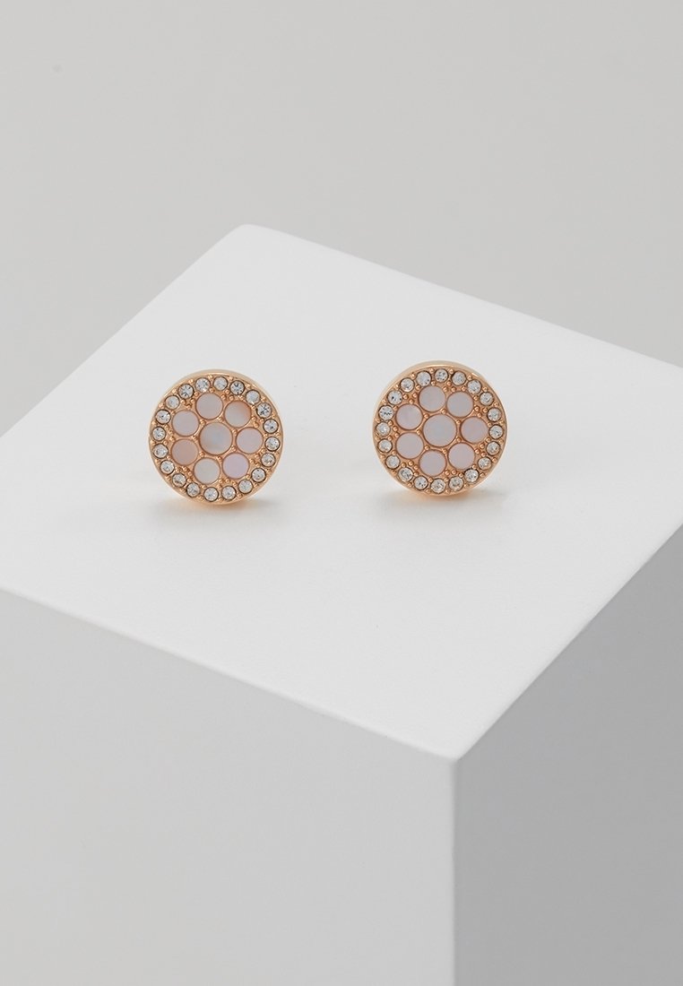 Boucles d'oreilles clous rondes en or avec centres en émail rose et strass clairs formant un motif circulaire sur un bloc d'exposition blanc.