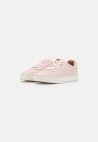 Paire de baskets basses rose clair avec semelles blanches et bordure festonnée sur les lacets sur fond blanc.