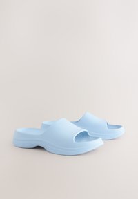 Sandales bleu clair à enfiler en plastique lisse, avec un design à bout ouvert et une semelle profilée avec des lignes horizontales subtiles.