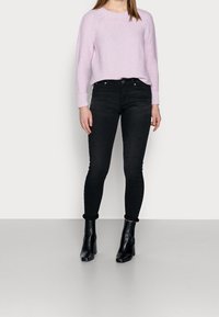 Suéter de punto rosa claro con puños acanalados, combinado con unos jeans skinny de cintura alta negros y botines negros de tacón.