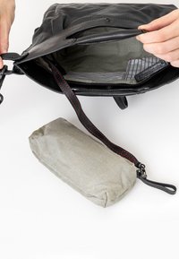 Schwarze Ledertasche mit gefüttertem Innenraum. Ausgestattet mit einem rot genähten Gurt und einem kleinen gestreiften Beutel. Mehrere Taschen, Reißverschluss und glatte Textur.