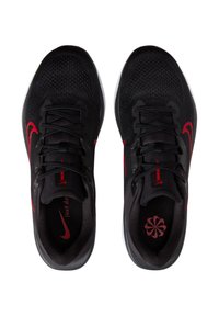 Zapatillas deportivas negras con parte superior de malla transpirable, acentos rojos en el swoosh y los cordones, y suela blanca. Superficie texturizada con detalle del logo.