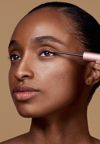 Eyeliner liquido in un contenitore rosa applicato sulla palpebra inferiore. Il soggetto ha la pelle liscia di un marrone medio e occhi marroni, con un trucco naturale.