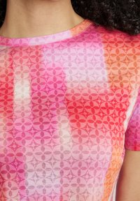 Camisa de manga corta en tejido ligero con un patrón degradado de rosa y naranja. Presenta motivos circulares y un cuello redondo.