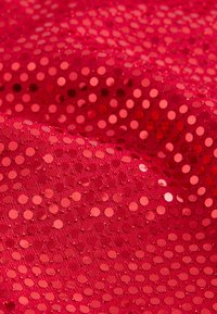 Rødt stof med en tekstureret overflade, der har skinnende, cirkulære palietter i forskellige størrelser, som skaber et mønster af reflekterende prikker.