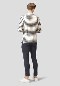 Camisa de manga larga a rayas en crema y azul marino, combinada con pantalones azul marino. Modelo con zapatillas blancas, visto desde la parte posterior sobre un fondo gris.