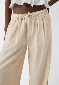 Lichtbeige wijdvallende broek gemaakt van een gestructureerde stof, met een elastische tailleband met een trekkoord en zijzakken.