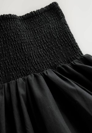 Sort kjole med en smocket overdel, med sammenrynket stof fra taljen og ned. Glat tekstur med en flydende silhuet.