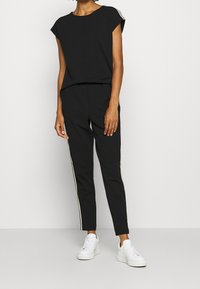 Czarny krótki top w połączeniu z czarnymi zwężającymi się spodniami z białymi bocznymi paskami. Uzupełniony białymi sneakersami. Gładki, lekki materiał.