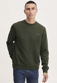 Donkergroen sweatshirt van katoen met een ronde hals, geribbelde boorden en een klein logo op de borst. Draagt in combinatie met blauwe spijkerbroek.