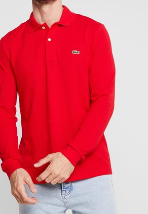 Polo-shirt rouge à manches longues en coton, avec un col classique, une patte de boutonnage à trois boutons et un petit logo vert sur la poitrine gauche.