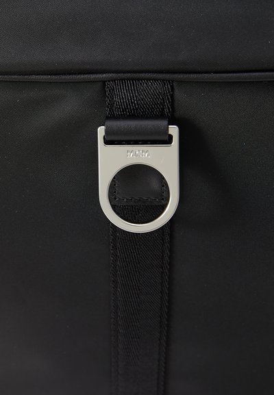Black textile bag featuring a circular silver hardware detail. The design includes a sturdy strap and a smooth finish.