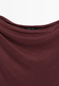 Miękki bordowy materiał z szerokim, drapowanym dekoltem i małą czarną metką z napisem „Massimo Dutti, Made in Cambodia.”