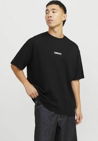 Sort bomulds T-shirt med korte ærmer, som har et hvidt "CARE90" logo på brystet. Stoffet har en glat, afslappet tekstur.