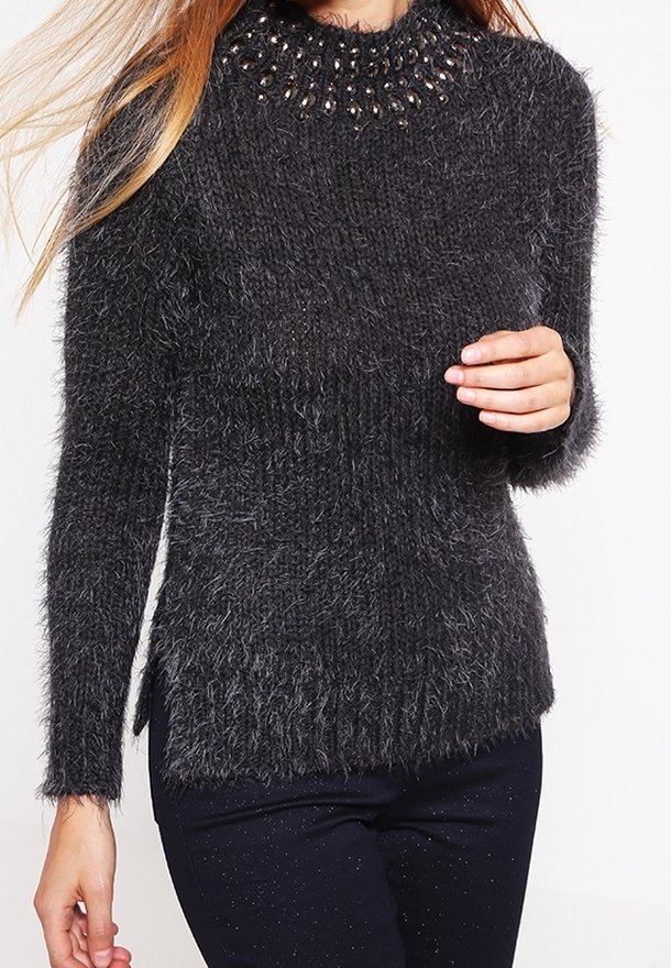Femme portant un pull en maille grise foncée et duveteuse avec un col arrondi orné et des manches longues, associé à un pantalon foncé.