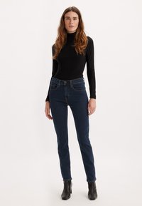 Jeans skinny blu scuri con vita alta, design aderente e classico stile a cinque tasche. Abbinati a un top nero a maniche lunghe e stivaletti neri.