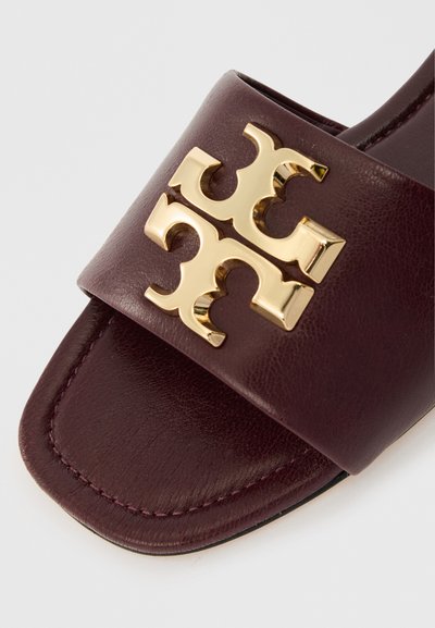 Σκούρο μπορντό δερμάτινο σανδάλι με τετράγωνη μύτη και μεγάλη λαμπερή χρυσή διακόσμηση με διπλό Τ στο λουρί.