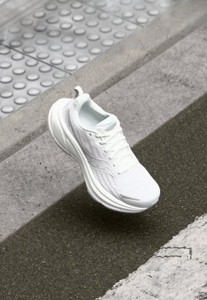 Chaussure de sport blanche avec une tige en maille, un design texturé et une semelle épaisse. Présente une boîte à orteils lisse et un système de laçage.