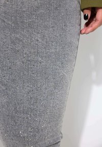 Jeans de mezclilla gris con una textura brillante y pequeños tachuelas doradas distribuidas uniformemente por la tela, diseño ajustado y acabado suave.