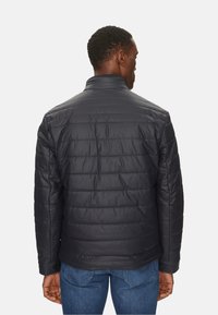 Chaqueta negra acolchada con un alto cuello, diseño acolchado y textura suave. Costuras visibles que acentúan la silueta ajustada.
