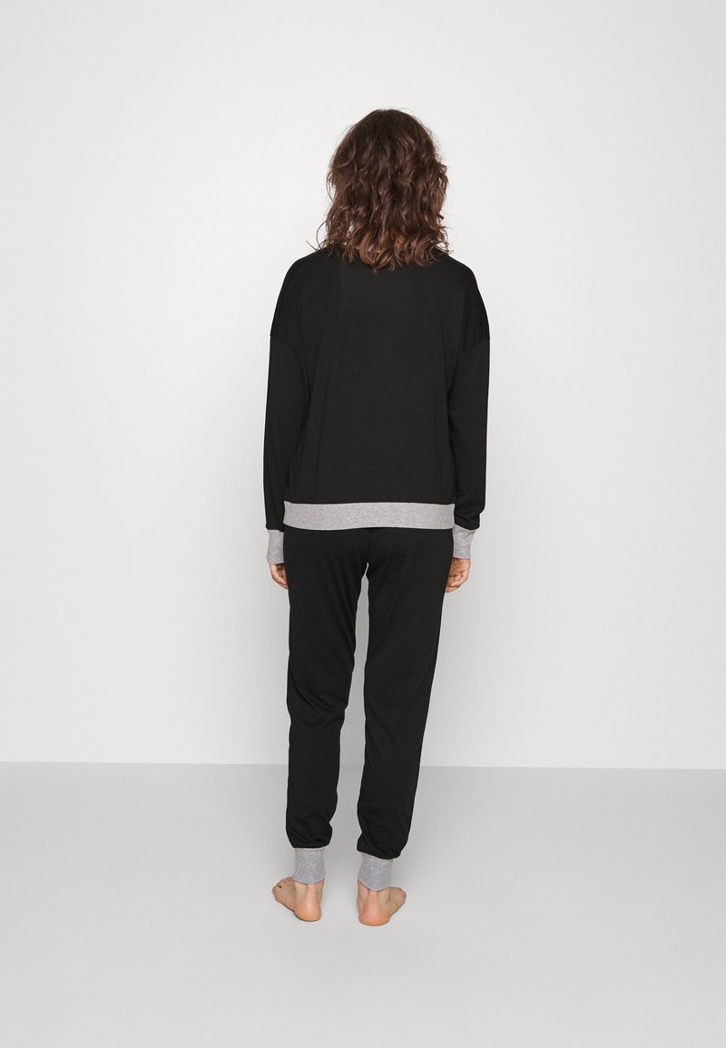 Conjunto de loungewear negro que incluye una camiseta de manga larga de corte relajado con acentos grises y pantalones a juego con puños elásticos. Tejido suave, diseño minimalista.