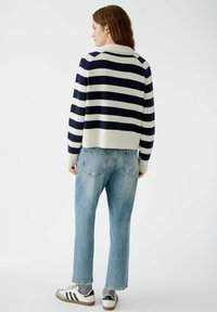 Gestreifter Strickpullover in Marineblau und Creme, mit hohem Kragen und geripptem Saum. Kombiniert mit hellblauen, geraden Jeans und weißen Sneakers.