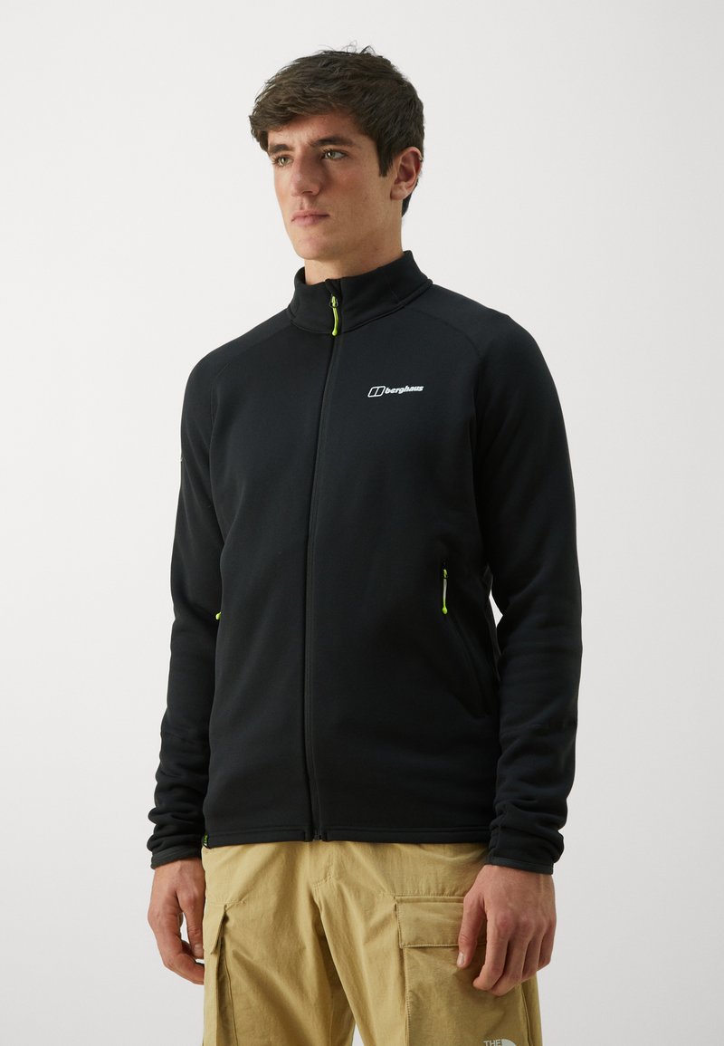 Giacca in pile nera con zip, colletto alto, dettagli verdi sulla zip e logo sul lato sinistro del petto; tessuto testurizzato per calore e comfort.