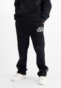 Zwarte trainingsbroek met een spetterverf ontwerp in blauw en geel; heeft het logo "BLACK BANANA" in het wit op de dij; elastische tailleband.