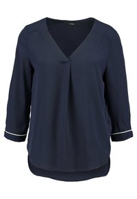 Chemisier bleu marine à manches trois-quarts, décolleté en V et léger pli à l'avant. Présente un passepoil blanc aux poignets et un ourlet arrondi.