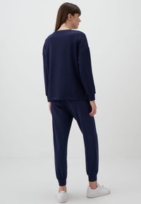 Granatowy sweter i dresy wykonane z mieszanki bawełny, z prążkowanymi mankietami i luźnym krojem, zestawione z białymi sneakersami.