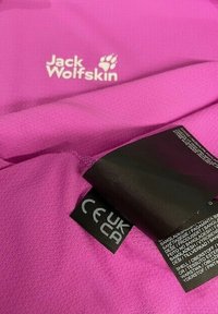 Tissu rose Jack Wolfskin avec étiquette d'entretien affichant les marques de conformité UK et CE.
