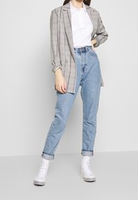 Gray plaid blazer with double-breasted buttons, paired with a white polo and high-waisted light blue jeans. Canvas sneakers.