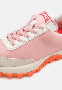 Ljusrosa lädersneakers med mockadetaljer, vit sömnad, rosa snören och en tydlig orange gummisula med ett texturerat mönster.