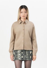 Beige button-up shirt with a collar, featuring seven buttons, paired with a textured black and white snake-print skirt. Smooth fabric.
