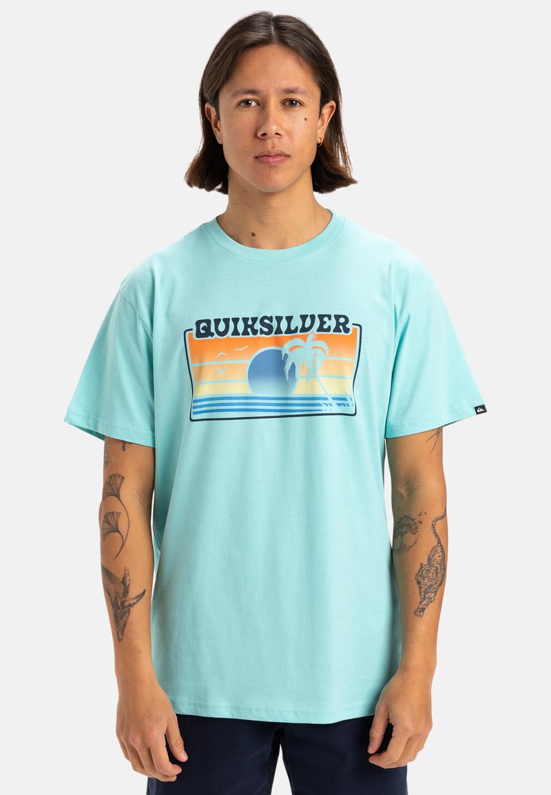 Camiseta de algodón turquesa con un estampado gráfico que presenta un diseño de atardecer y palmera. Manga corta y estilo de cuello redondo.