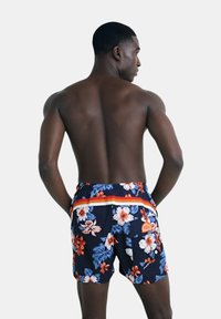 Costumi da bagno floreali blu navy con cintura a righe arancioni e bianche. Realizzati in tessuto leggero con una texture liscia e doppie tasche posteriori.