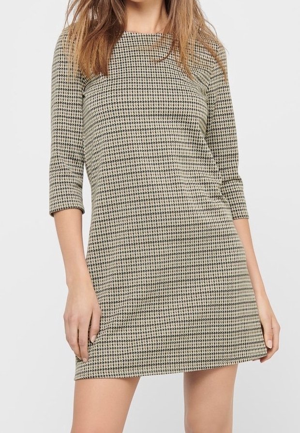 Kontrollerad klänning i beige och svart, med ärmar som når till armbågen och en rak silhuett. Texturerad tyg med ett subtilt mönster.