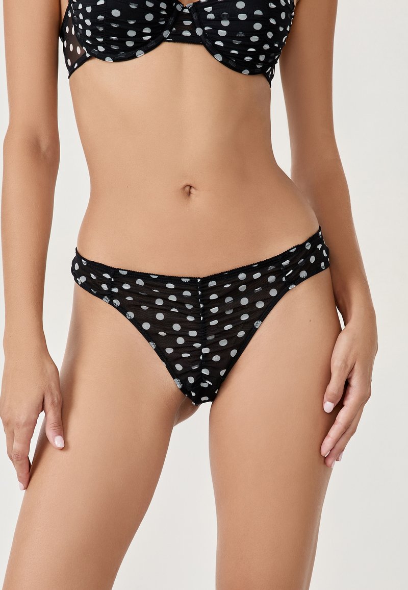 Tanga negro de malla con un patrón de lunares en gris. Tela semitransparente con una textura suave y cinturilla elástica.