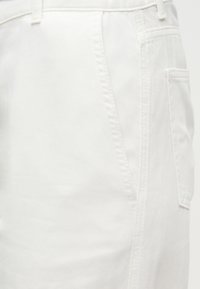 Κοντινή λήψη λευκού υφάσματος τζιν με εμφανή ραφή στο πλάι, θηλιά ζώνης και λεπτομέρειες πίσω τσέπης.